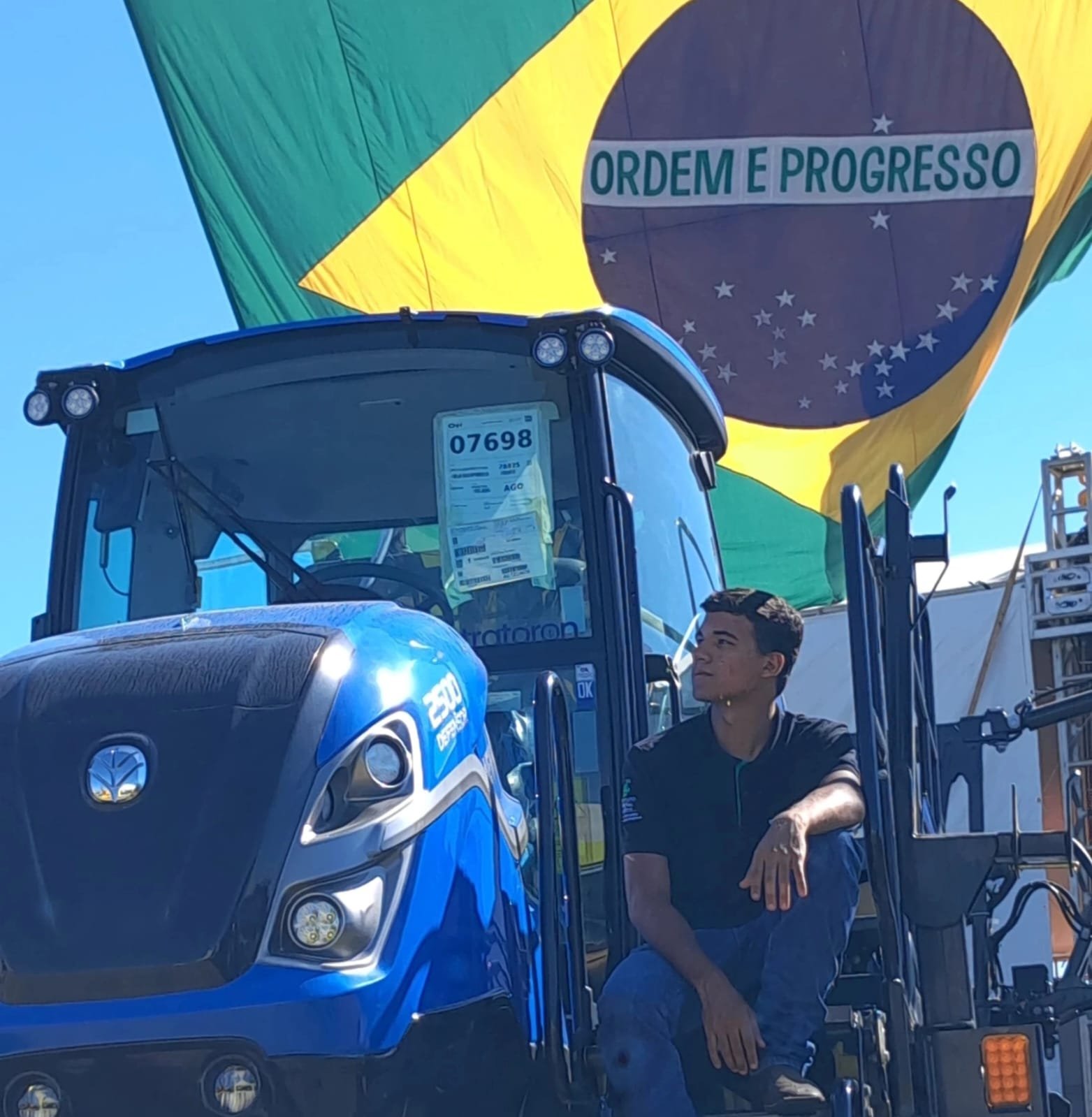 Rhuan próximo a um trator diante de uma grande bandeira do Brasil